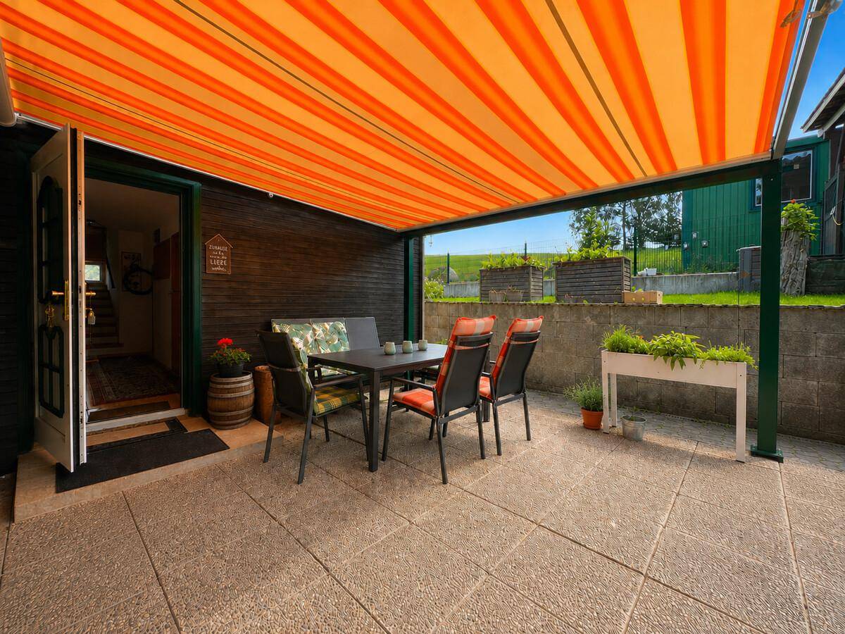 Überdachte Terrasse mit Gartenmöbeln und orange-gestreifter Markise, ideal für Mahlzeiten im Freien.
