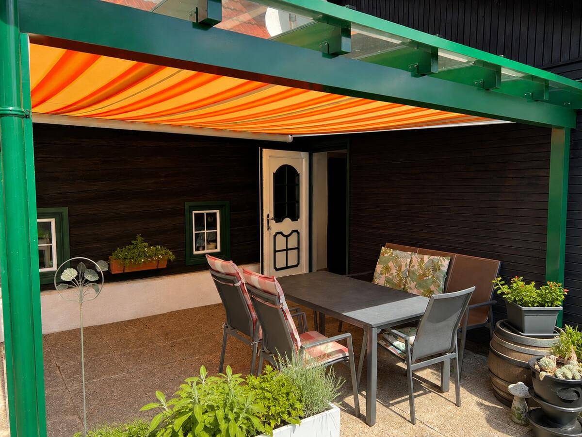 Überdachter Terrassenbereich mit Sitzgelegenheiten und Zugang zum Haus, umgeben von Pflanzen.