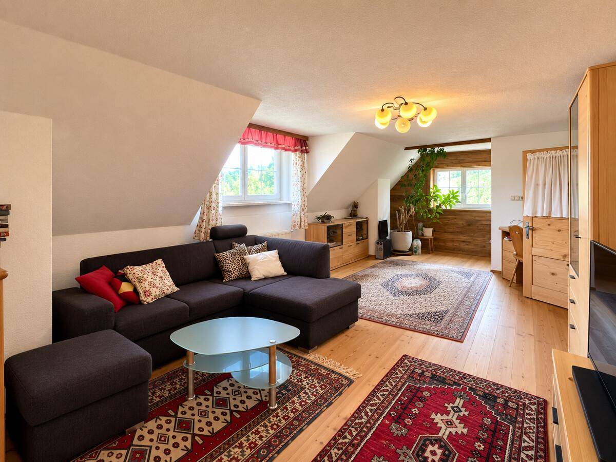 Geräumiges Wohnzimmer im Dachgeschoss mit Holzboden, gemütlicher Couch und Teppichen.