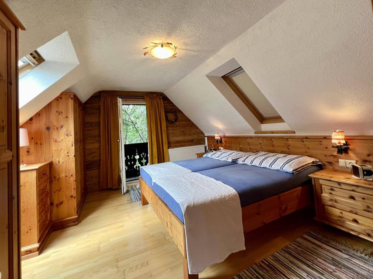 Schlafzimmer im Dachgeschoss mit Holzboden, Dachfenster und Zugang zu einem kleinen Balkon.