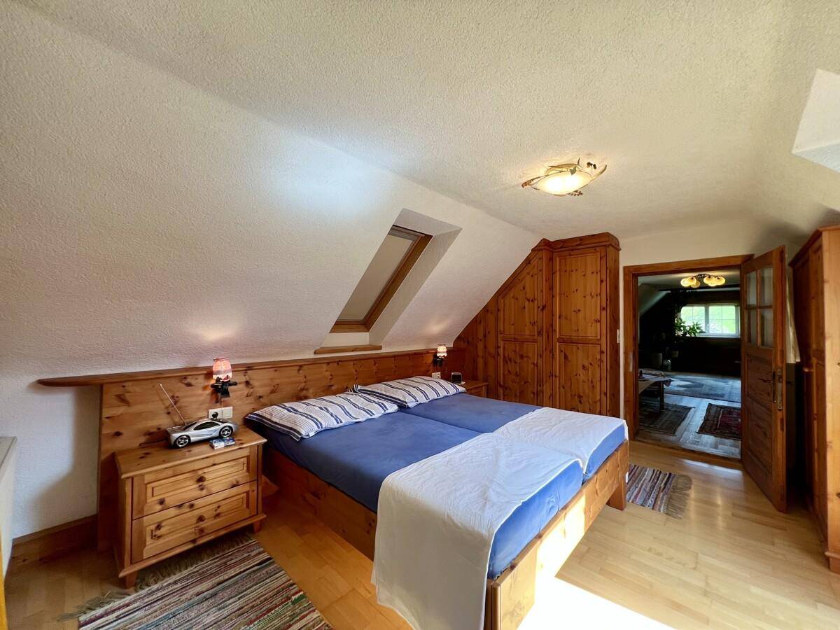 Helles Schlafzimmer im Dachgeschoss mit Doppelbett, Holzmöbeln und Dachfenster.