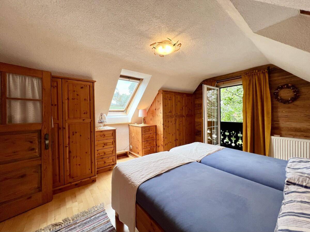 Gemütliches Schlafzimmer im Dachgeschoss mit Holzboden, Dachfenster und Zugang zum Balkon.