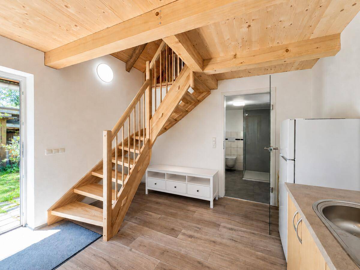 Offener Wohnbereich mit Holztreppe, Zugang zum Bad und Blick in den Garten.