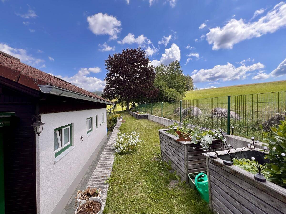 Gepflegter Gartenweg entlang des Hauses mit Hochbeeten und weitem Blick.