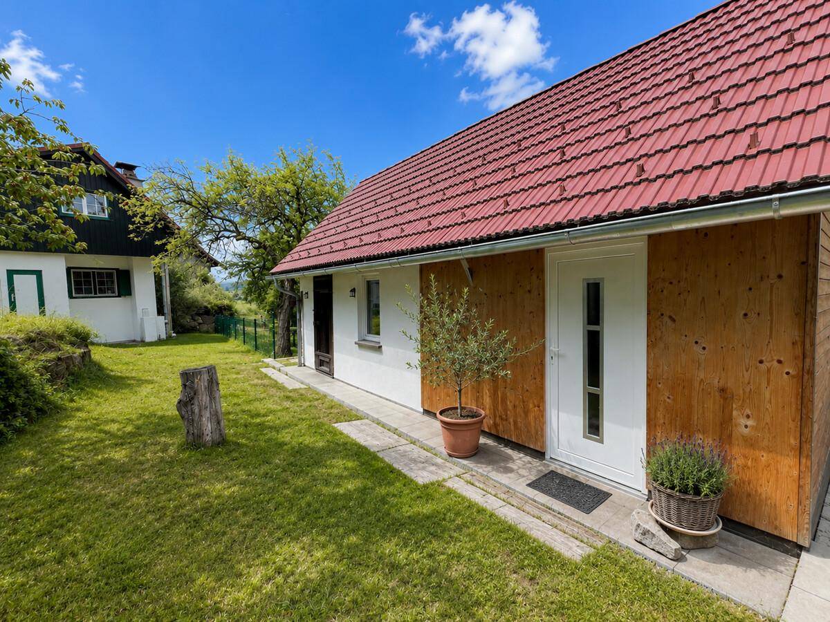 Charmantes Landhaus mit rotem Ziegeldach und Holzfassade, umgeben von Grün.