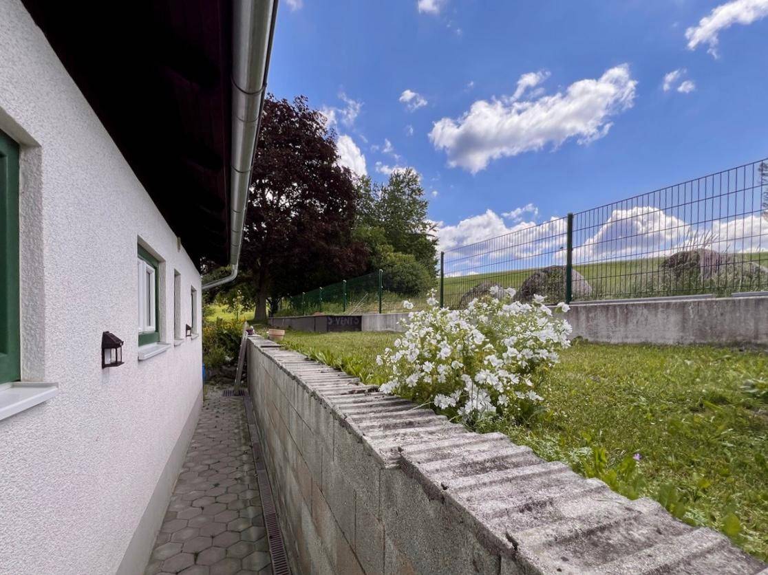 Seitlicher Gartenweg entlang des Hauses mit Blumenbeeten und Zaun.