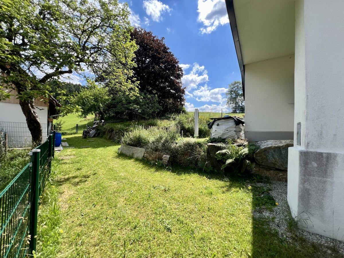 Rasenfläche neben dem Haus mit Steinbegrenzung und Blick ins Grüne.