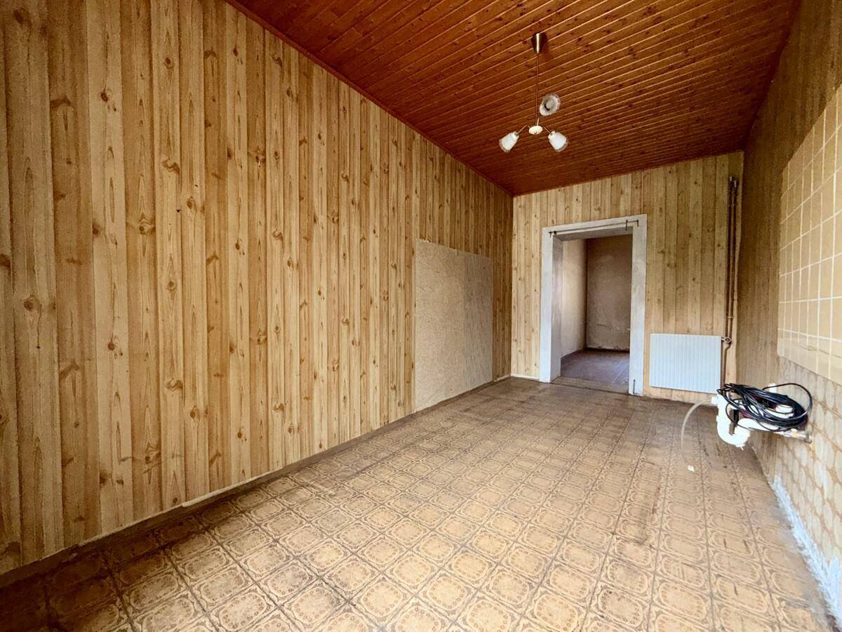 Raum mit Holzvertäfelung an Wänden und Decke, gemustertem Linoleumboden und sichtbaren Leitungen.
