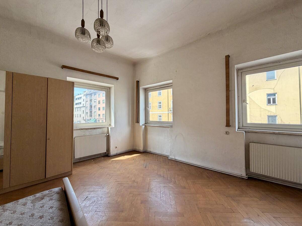 Helles Schlafzimmer mit Fischgrätparkett, mehreren Fenstern und einem Kleiderschrank.