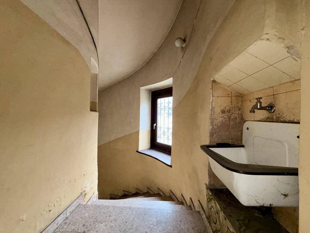 Treppenhaus mit einem kleinen Fenster, einem alten Waschbecken und abgenutzten Stufen.