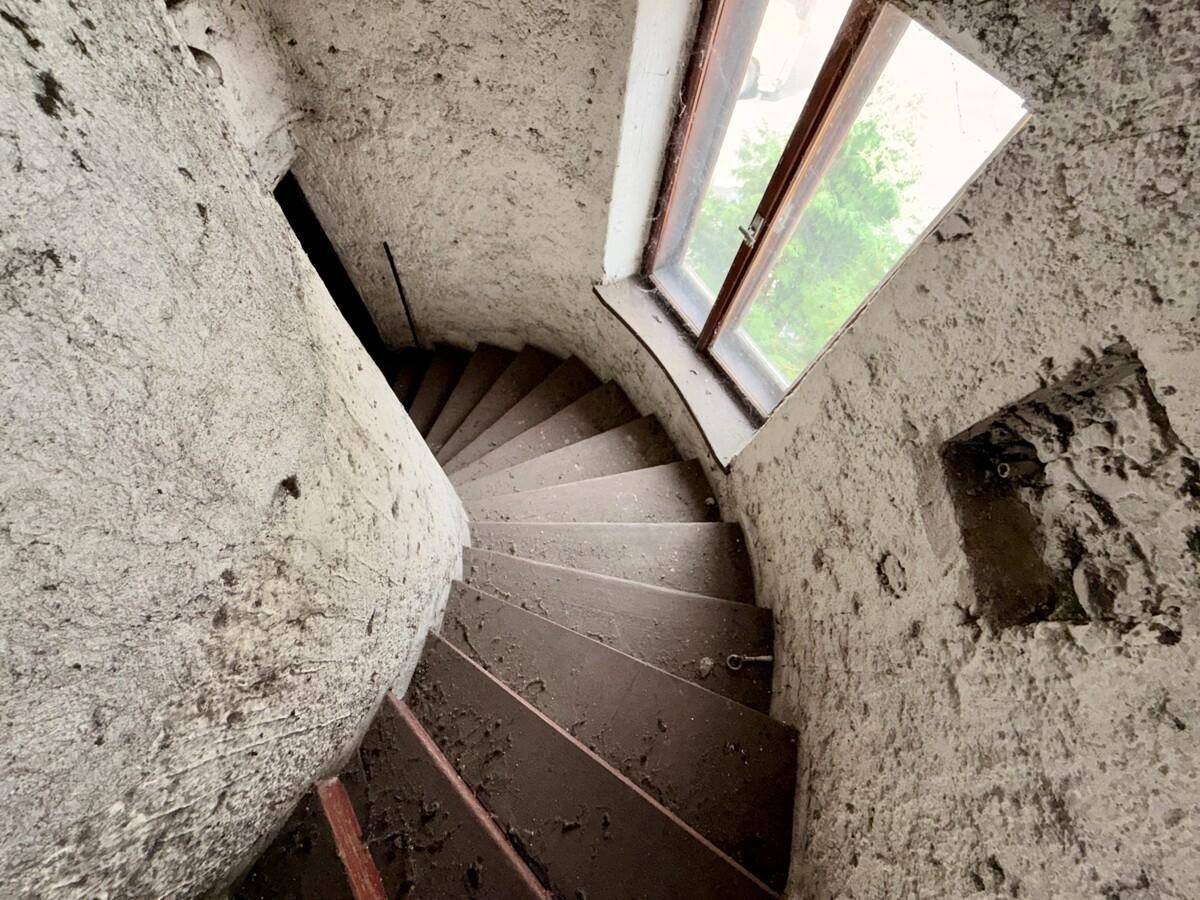 Wendeltreppe mit rauen Betonwänden und einem Fenster, das Licht in den Schacht bringt.