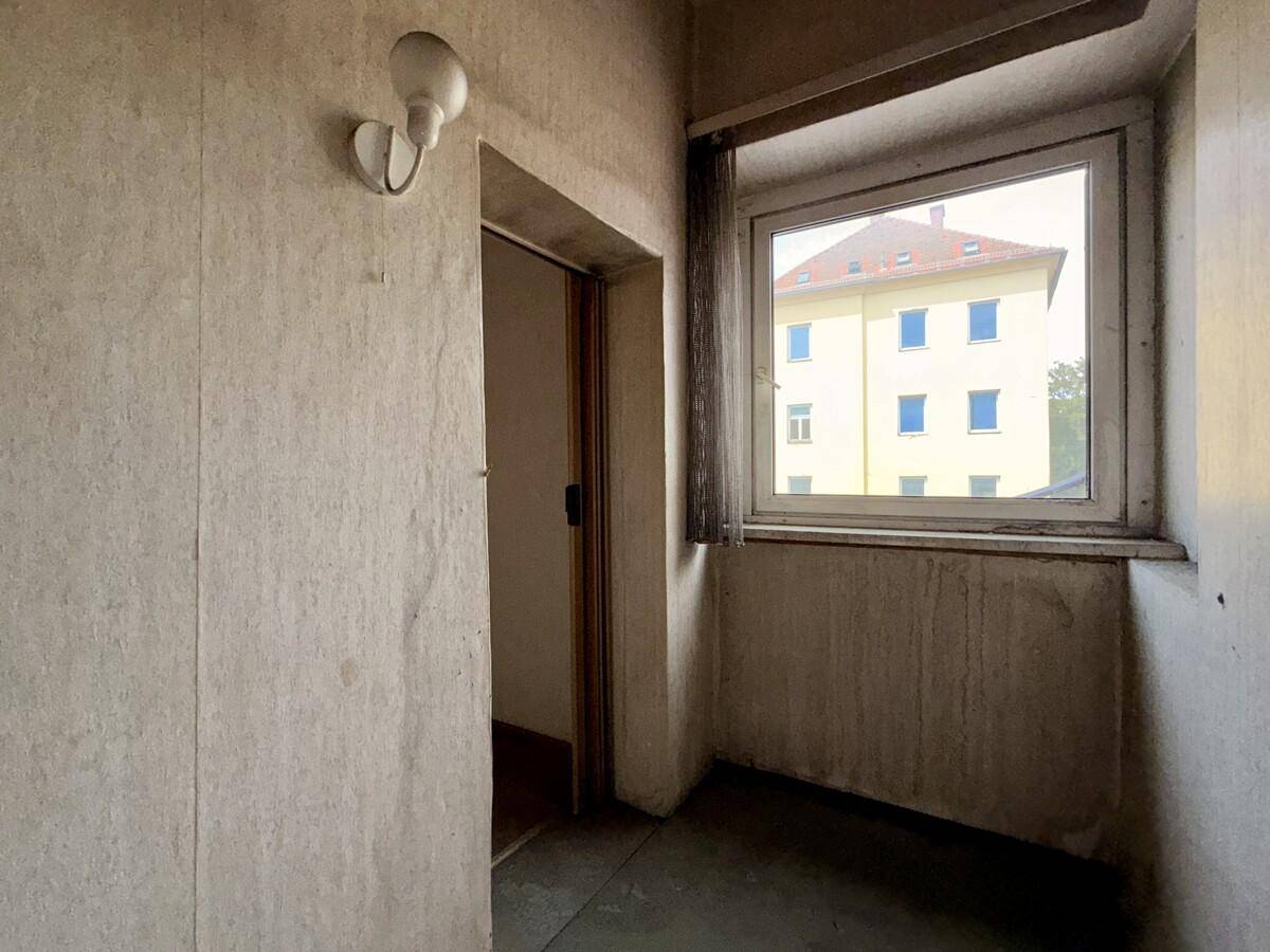 Kleiner Flurbereich mit einem Fenster, das Tageslicht hereinlässt, und abgenutzten Wänden.