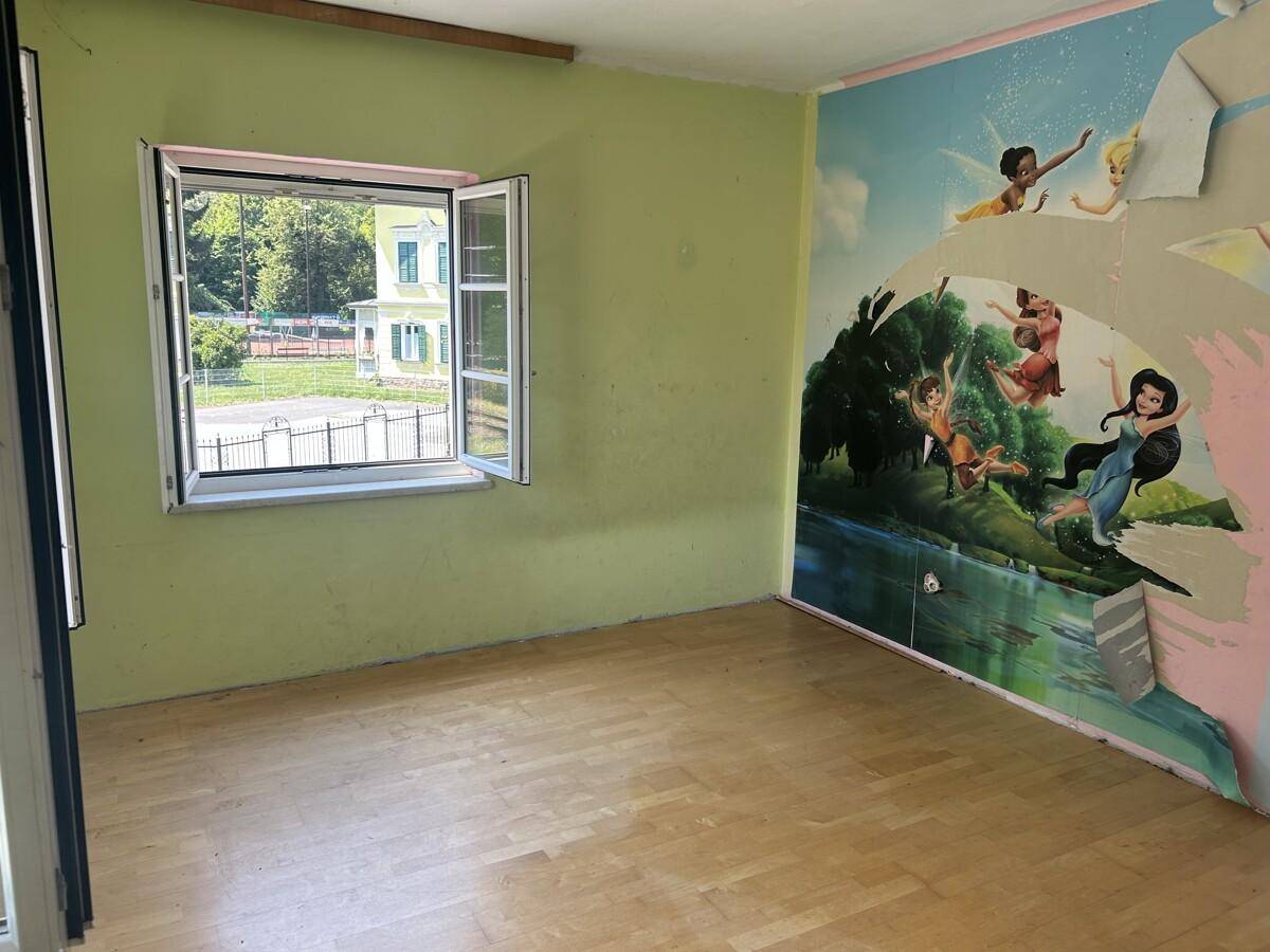 Kinderzimmer mit hellgrünen Wänden, Holzboden und einer farbenfrohen Wandmalerei.