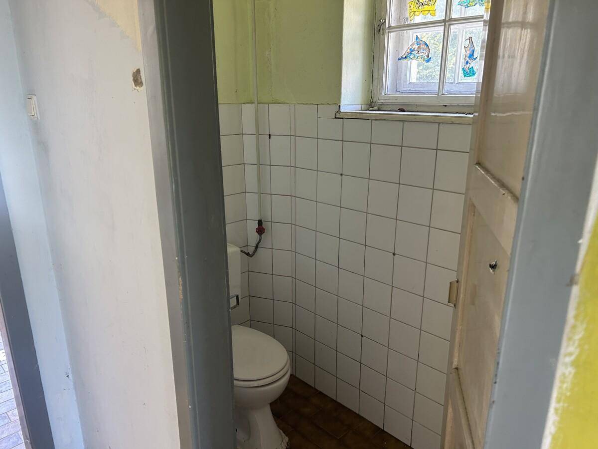 Kleines WC mit weißen Fliesen, Toilette und einem kleinen Fenster mit Buntglas.