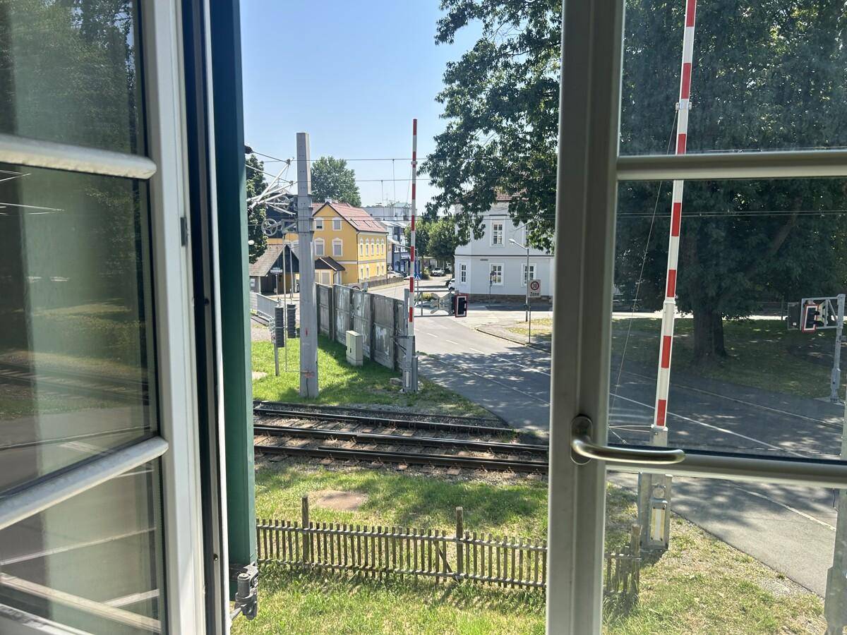 Blick aus dem Fenster auf Bahngleise, eine Schranke und die umliegende Bebauung.