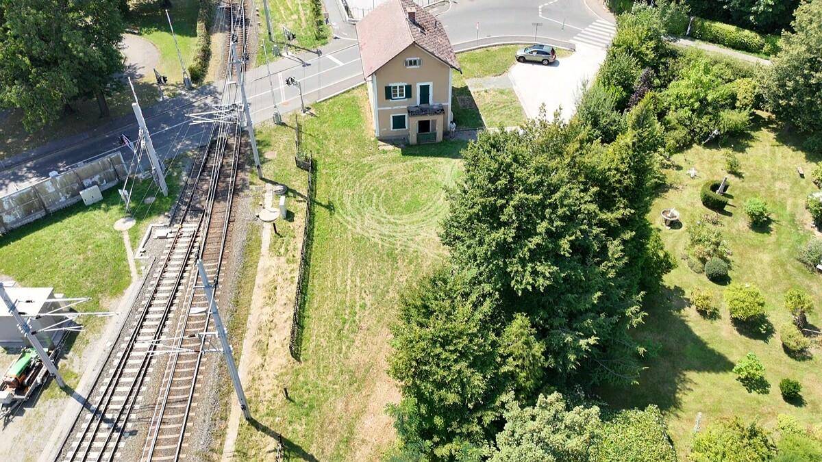Luftaufnahme eines Hauses neben Bahngleisen und einer Straße, umgeben von viel Grün.