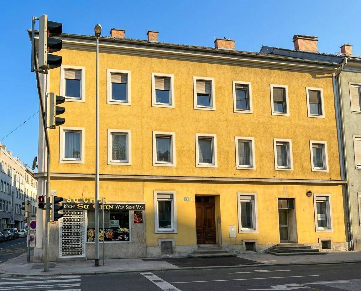 Gelbes Mehrfamilienhaus an einer Straßenecke mit Geschäften im Erdgeschoss.