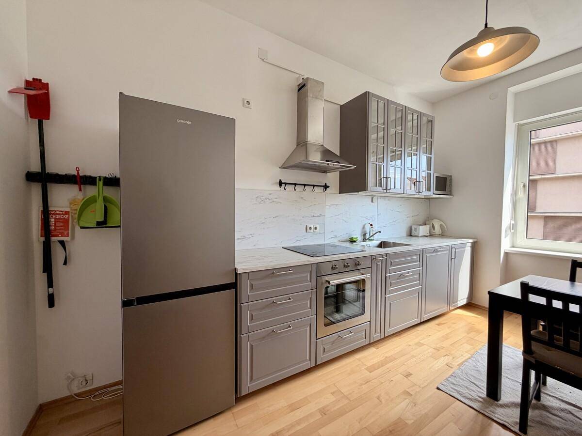 Funktionale Küche mit Edelstahlkühlschrank, Kochfeld und Essbereich am Fenster.