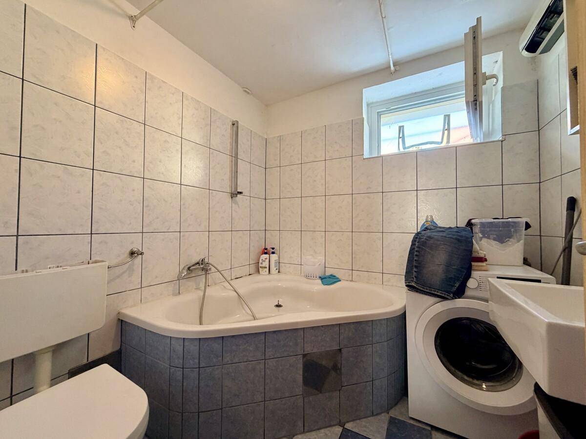 Badezimmer mit Eckbadewanne, WC, Waschmaschine und hellblauen Fliesen.