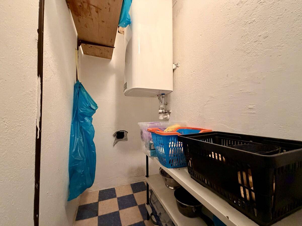 Kleiner Abstellraum mit Regalen, einem Warmwasserbereiter und kariertem Fliesenboden.