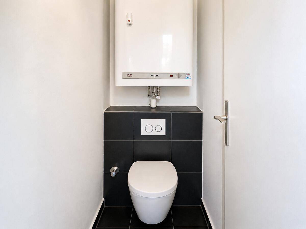 Separates WC mit wandhängender Toilette und einem Warmwasserbereiter an der Wand.