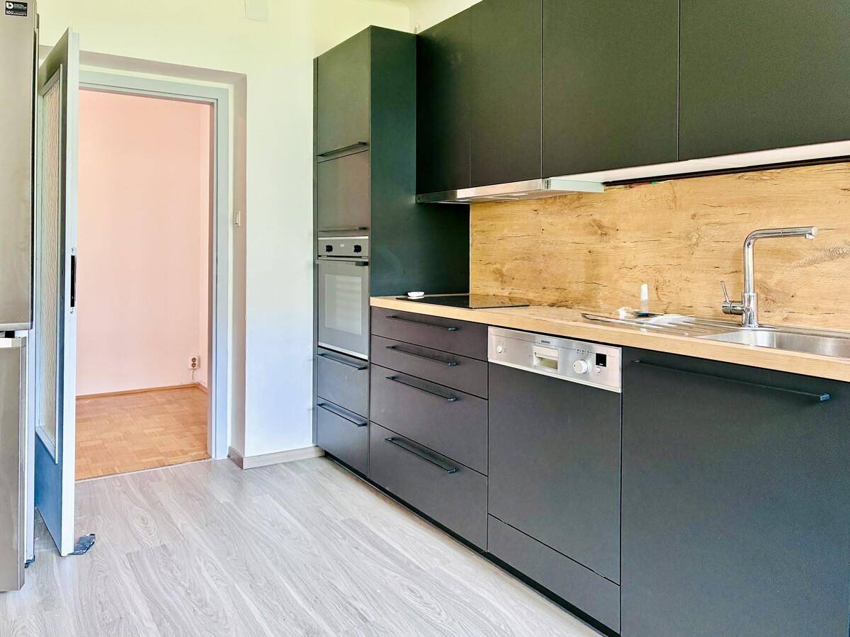 Funktionale Küche mit dunklen Einbauschränken, modernen Geräten und Zugang zu einem weiteren Zimmer.