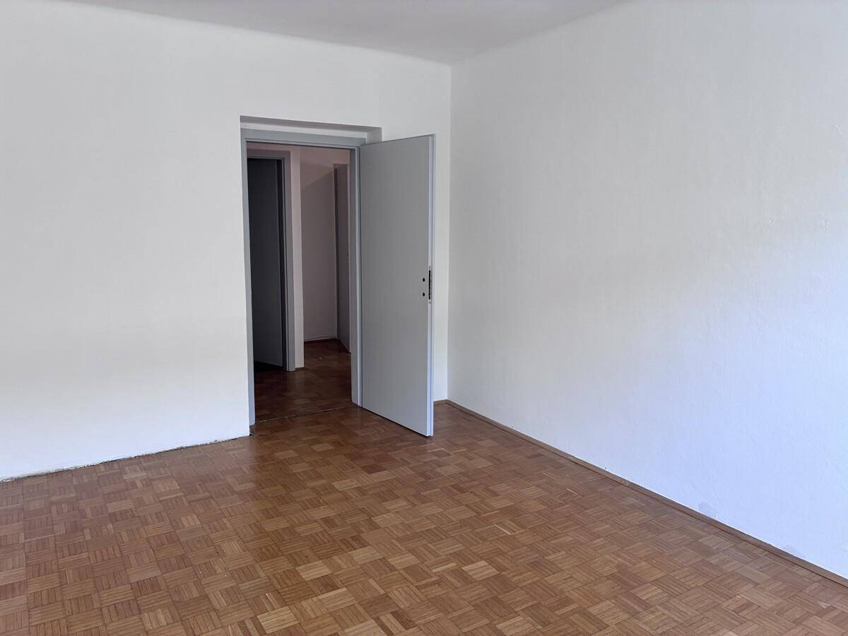 Helles Zimmer mit Parkettboden und Zugang zu einem langen Flur.