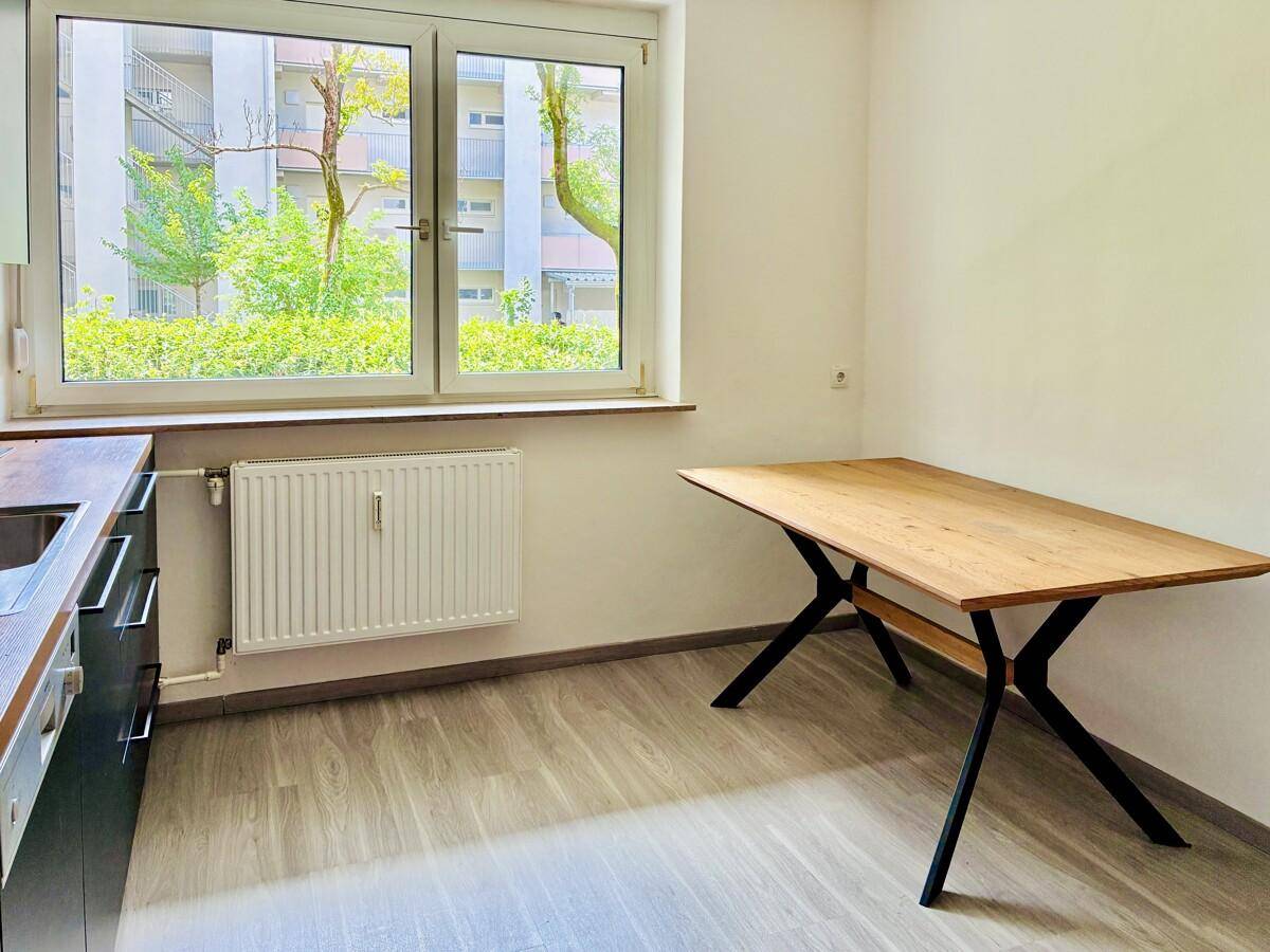 Heller Essbereich in der Küche mit Holztisch und großem Fenster mit Blick auf die umliegenden Gebäude.
