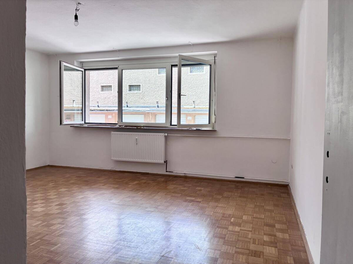 Geräumiges Wohnzimmer mit Parkettboden und großem Fenster, das viel Tageslicht hereinlässt.