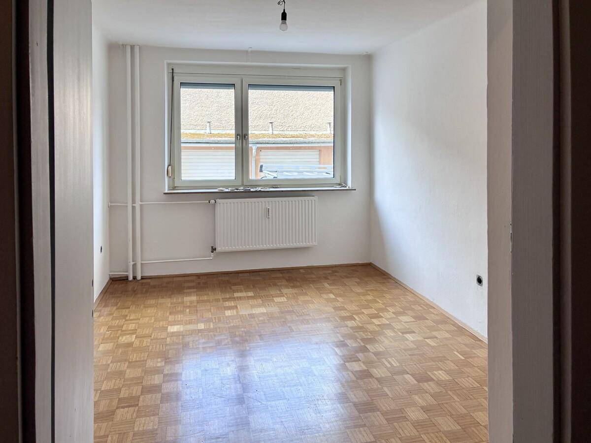 Helles Zimmer mit Parkettboden und Fenster, ideal als Schlaf- oder Arbeitszimmer nutzbar.