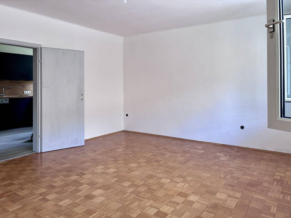 Helles Zimmer mit klassischem Parkettboden und Zugang zur modernen Küche.