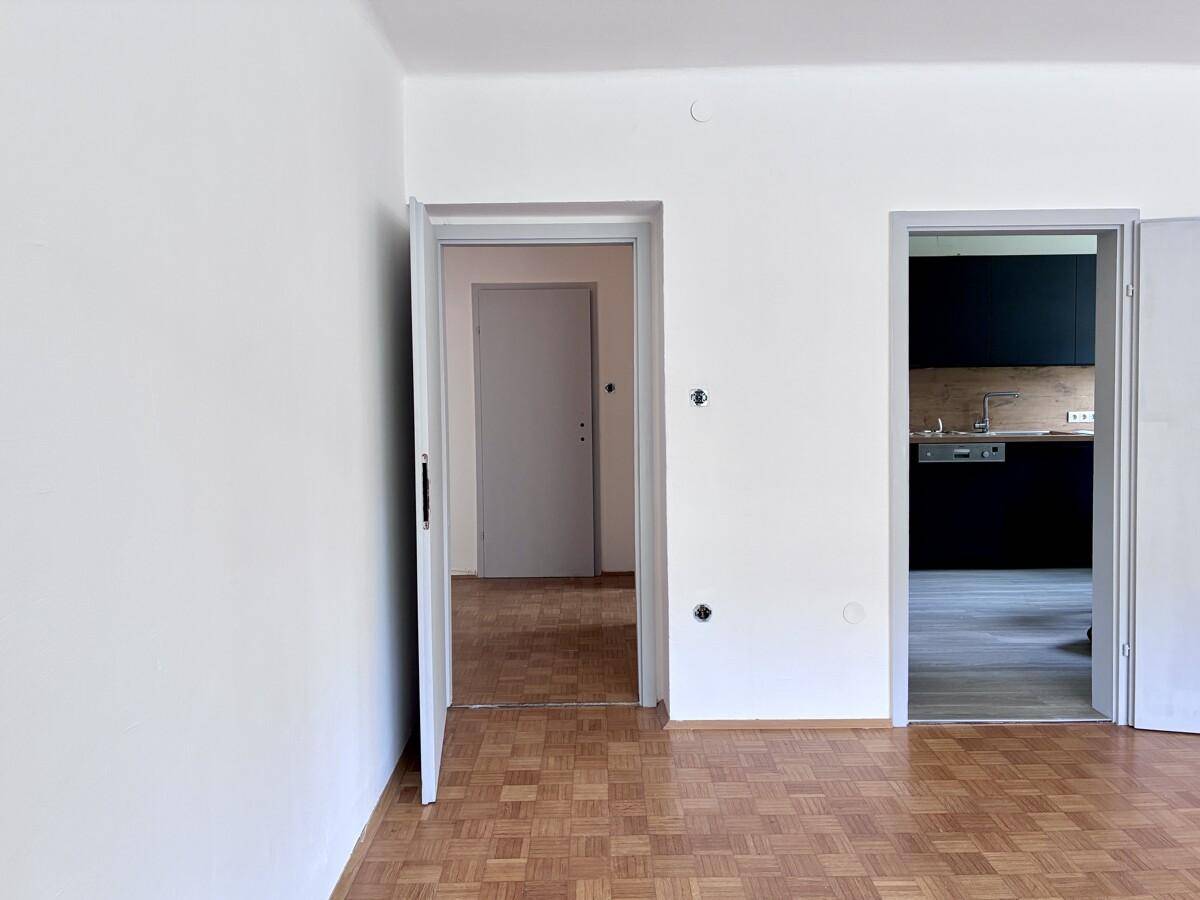 Geräumiges Zimmer mit Parkettboden und Zugang zur Küche sowie einem weiteren Raum.