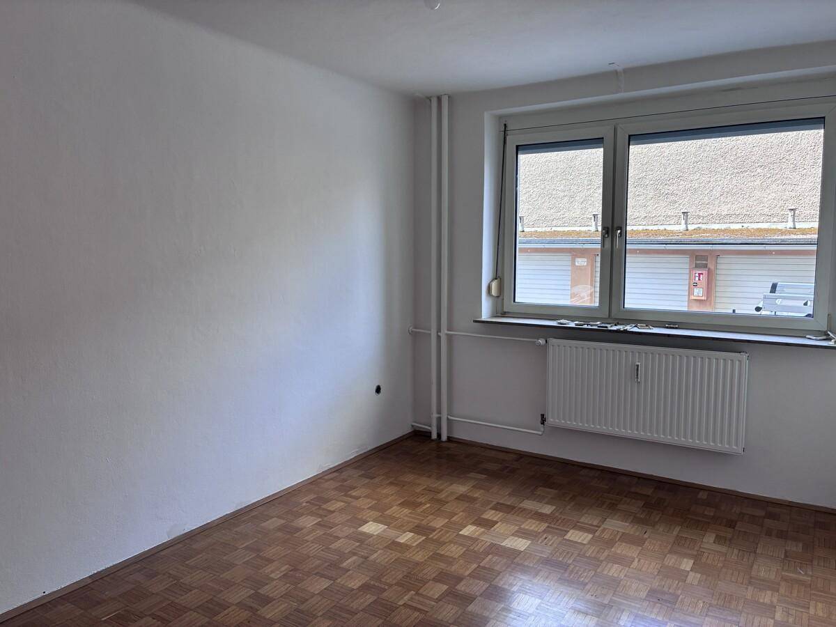 Geräumiges Zimmer mit Parkettboden und Fenster, das viel natürliches Licht hereinlässt.