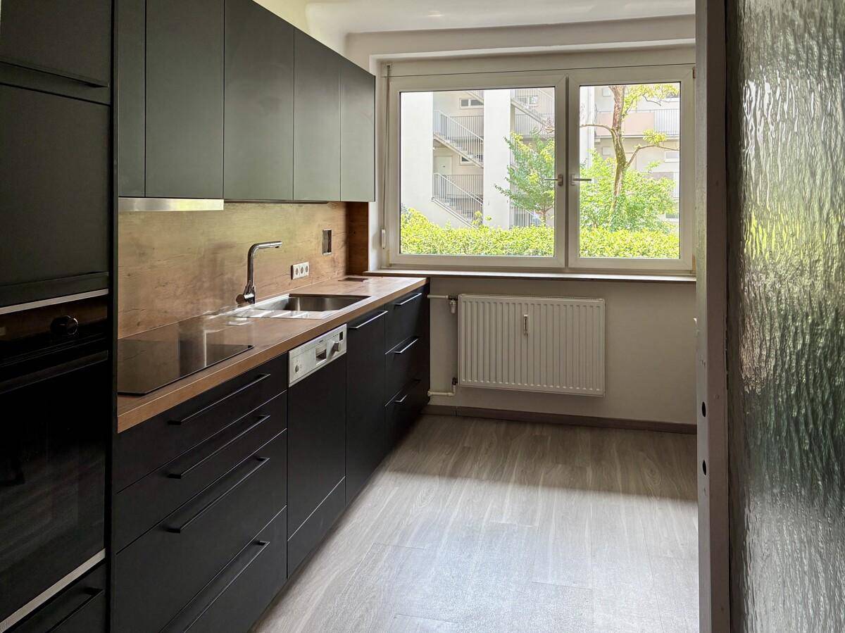 Moderne Einbauküche mit dunklen Fronten, integrierten Geräten und einem Fenster mit Blick ins Grüne.