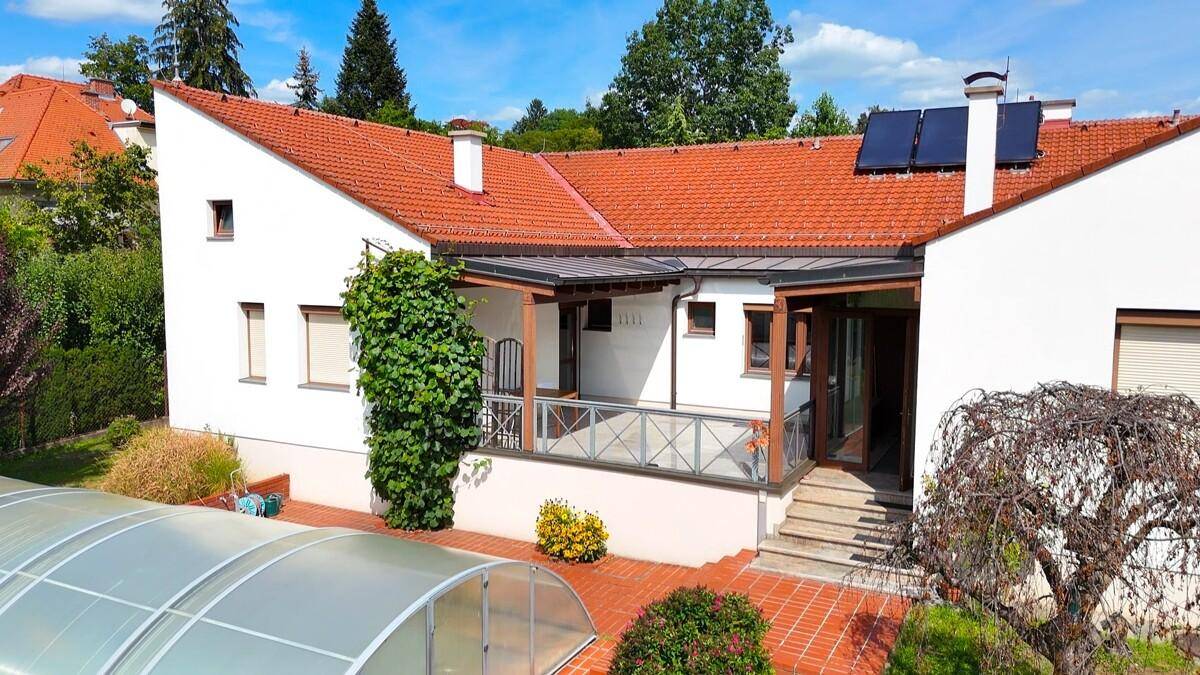 Detailansicht der Hausfassade mit überdachtem Poolbereich, Terrasse und Photovoltaikanlage auf dem Dach.