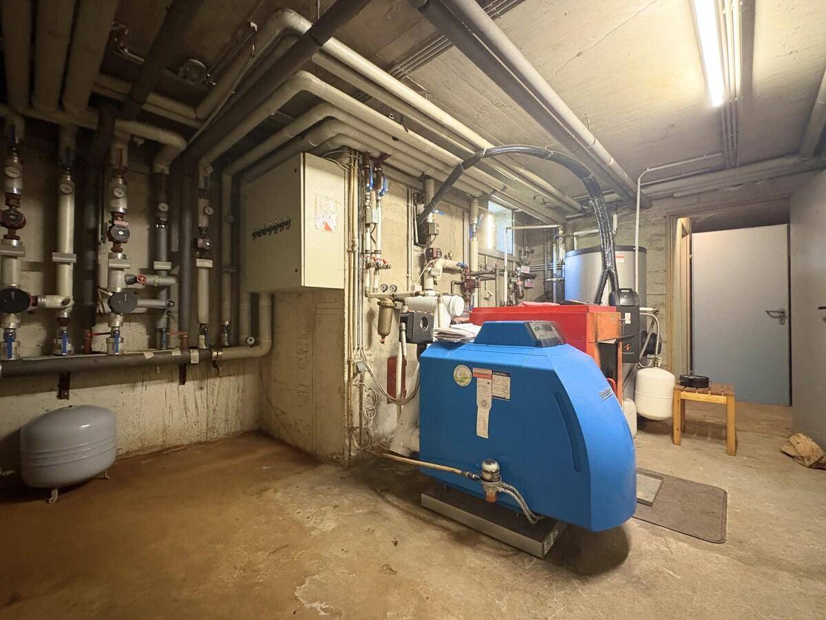 Heizungsraum mit umfangreicher Installation von Rohren und einem großen Heizkessel.