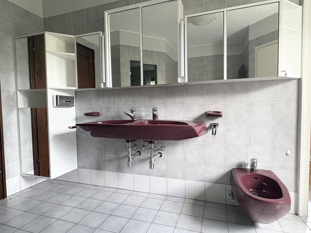 Badezimmer mit zwei Waschbecken, Bidet und Spiegelschränken, ausgestattet mit grauen Fliesen.