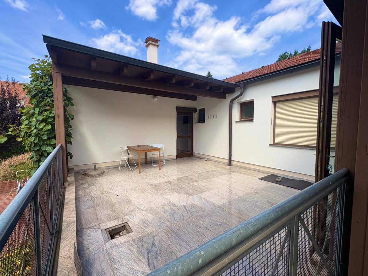 Überdachte Terrasse mit Steinfliesenboden und einfacher Möblierung, ideal für entspannte Stunden im Freien.