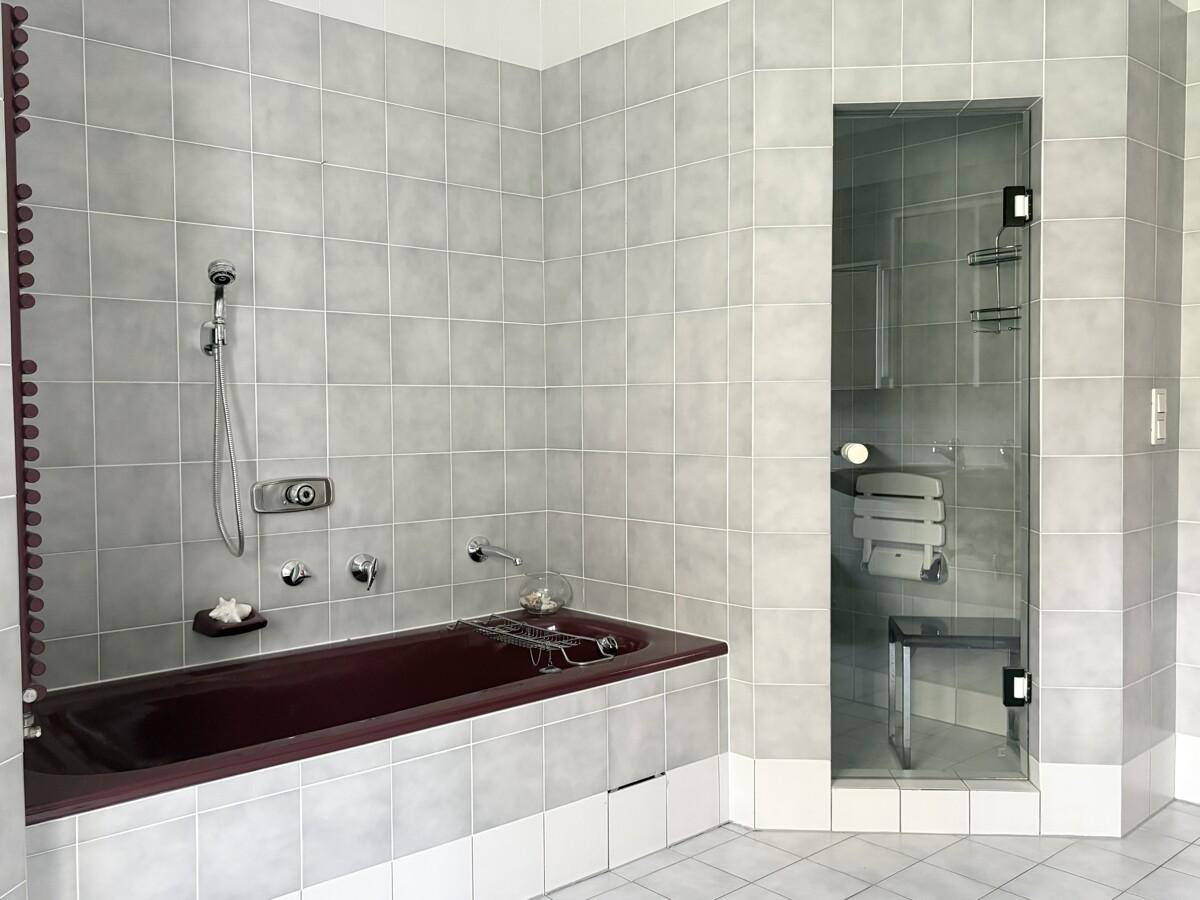 Geräumiges Badezimmer mit grauen Fliesen, einer Badewanne und einer begehbaren Dusche.