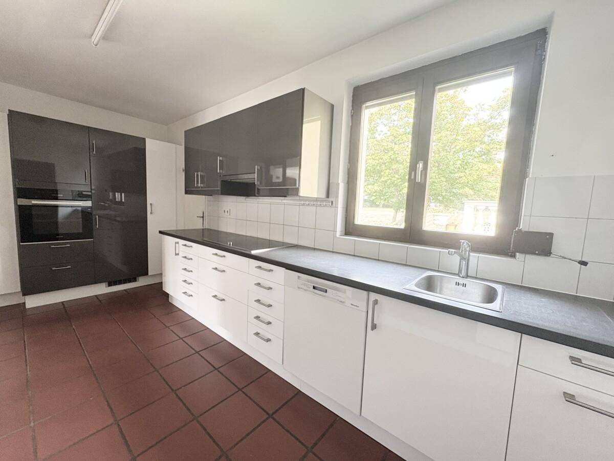 Helle Küche mit großem Fenster, weißen und grauen Schränken und integriertem Kochfeld.