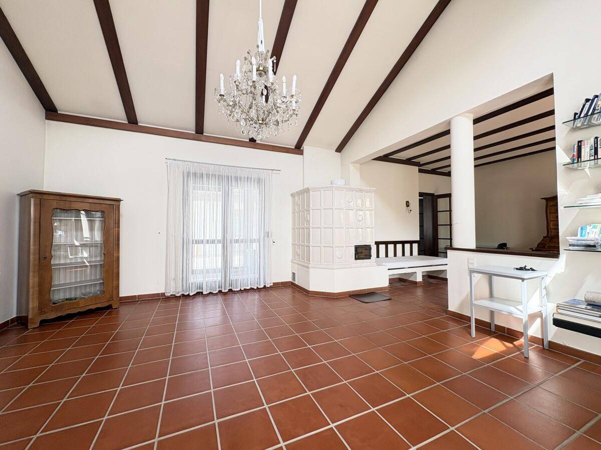 Helles Wohnzimmer mit Terrakottafliesen, Kachelofen und Zugang zu einem Balkon oder einer Terrasse.