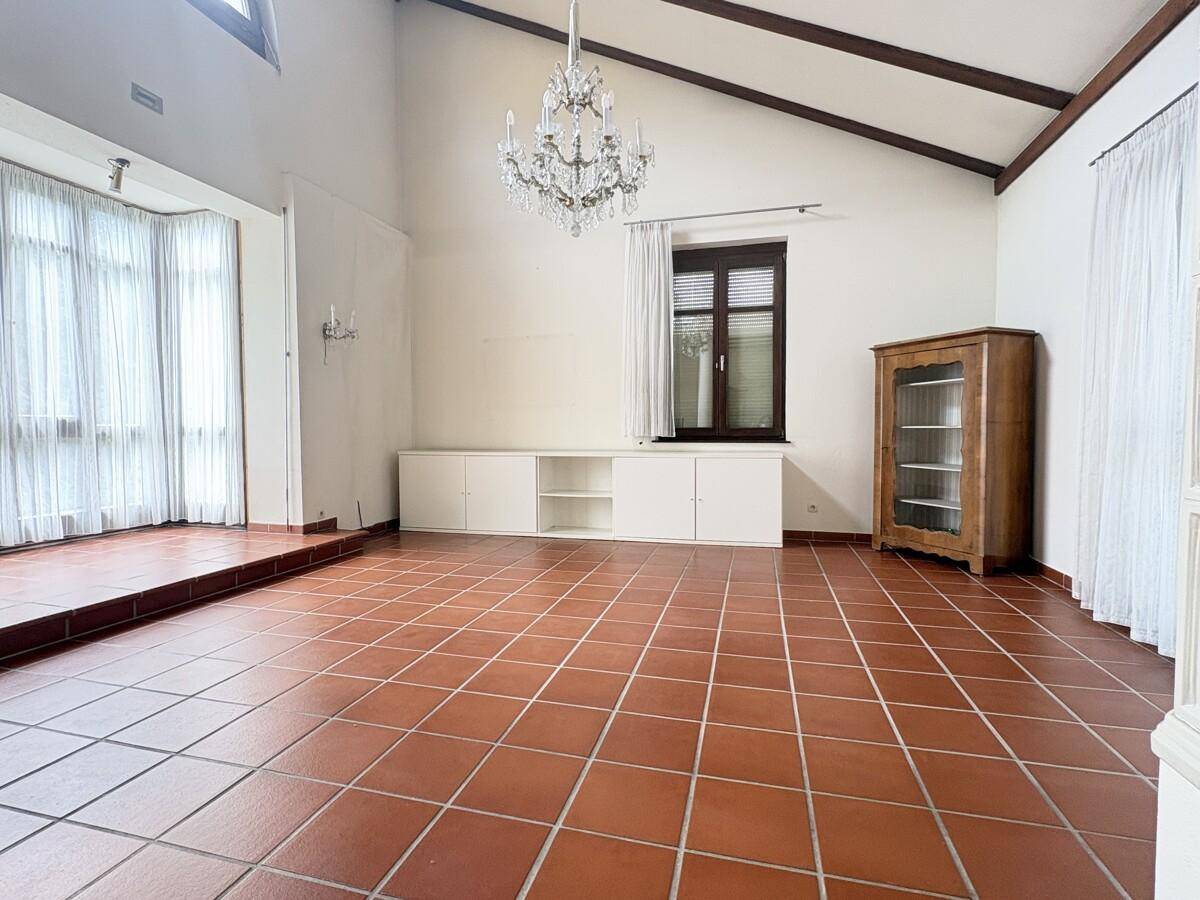 Großzügiges Wohnzimmer mit Terrakottafliesen, hohen Decken und einem dekorativen Kronleuchter.
