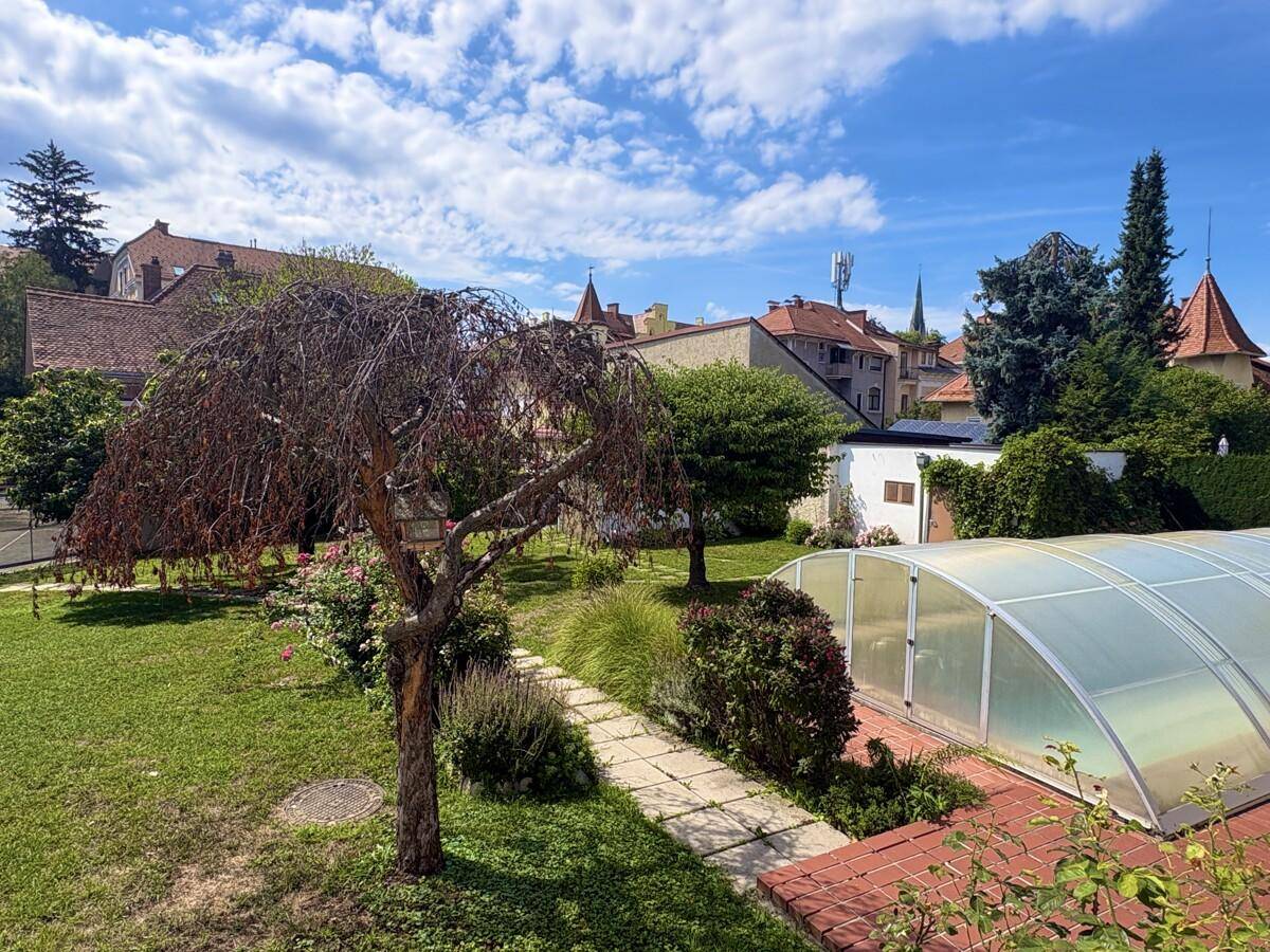 Weitläufiger Garten mit Rasenfläche, Bäumen und dem überdachten Swimmingpool.
