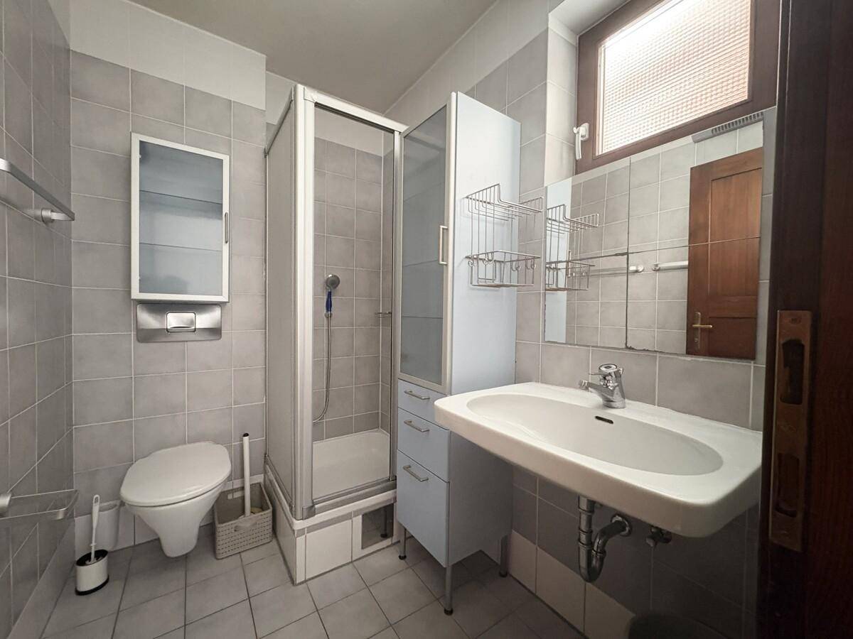 Kleineres Badezimmer mit Dusche, WC und Waschbecken, komplett gefliest in Grau.