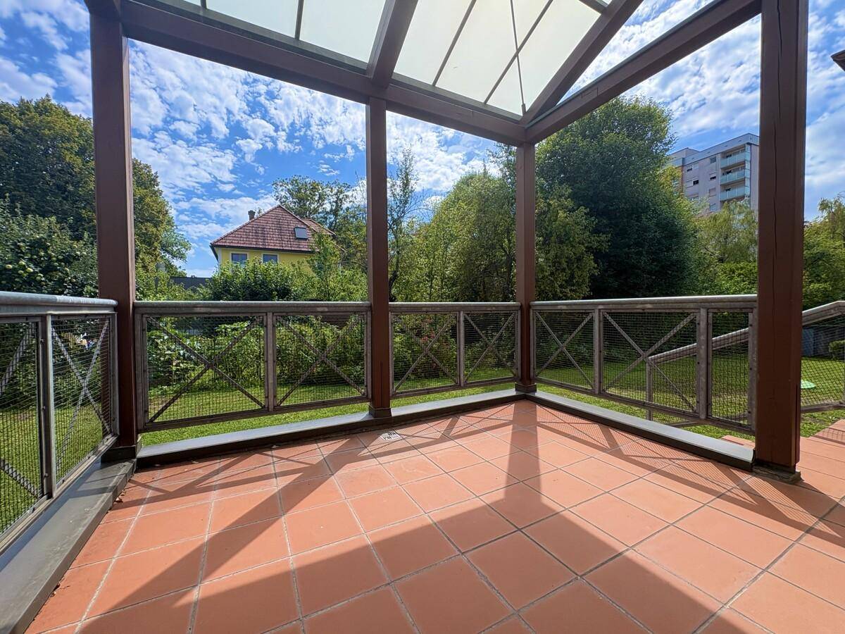 Überdachte Terrasse mit Terrakottafliesen und Blick ins Grüne, umgeben von einem Holzgeländer.