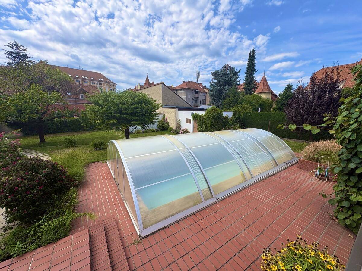 Überdachter Poolbereich mit angrenzender Terrasse und Blick auf den Garten und die Nachbarschaft.
