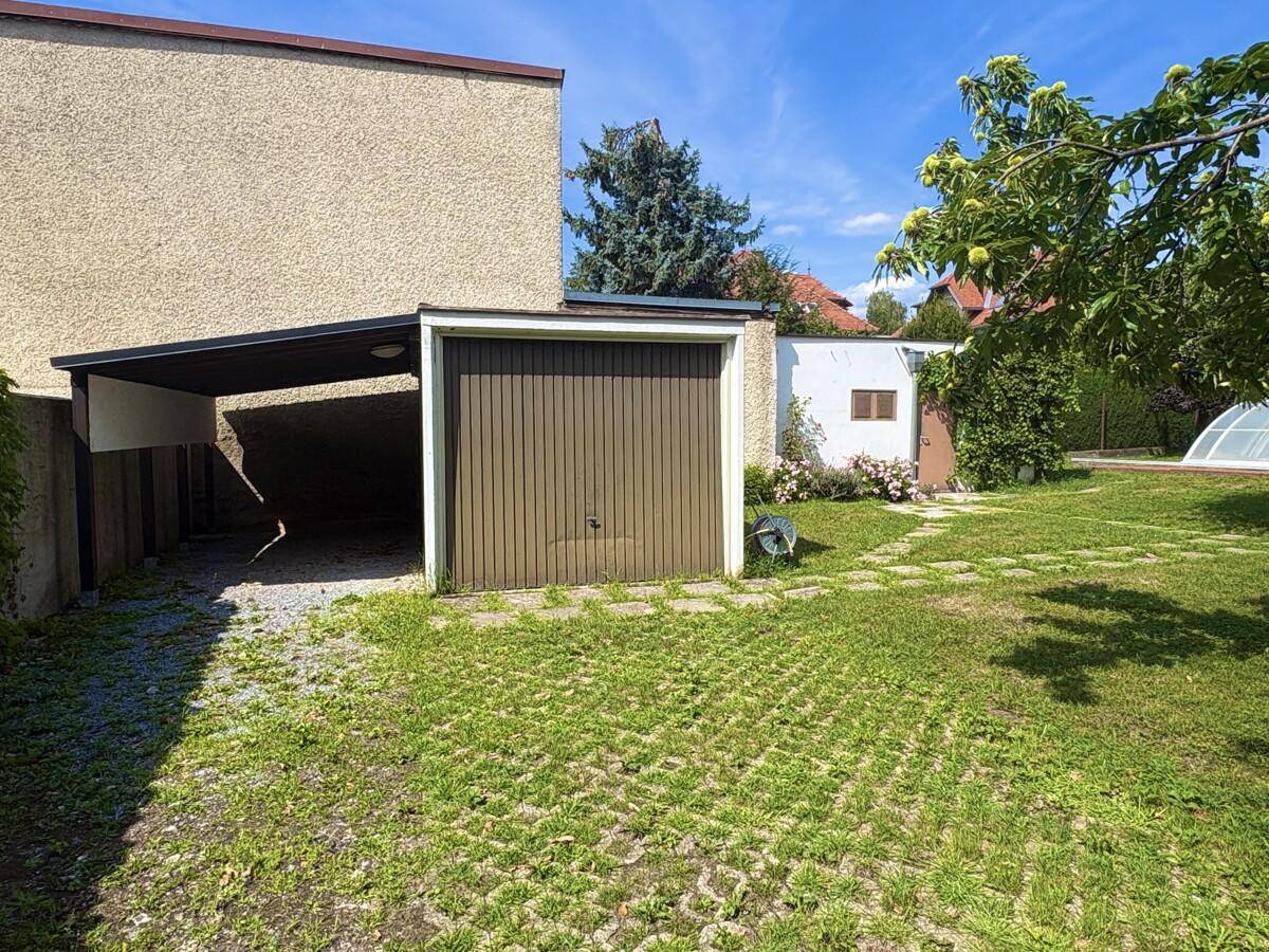 Einzelgarage mit Holzschwingtor und angrenzendem Carport auf dem Grundstück.