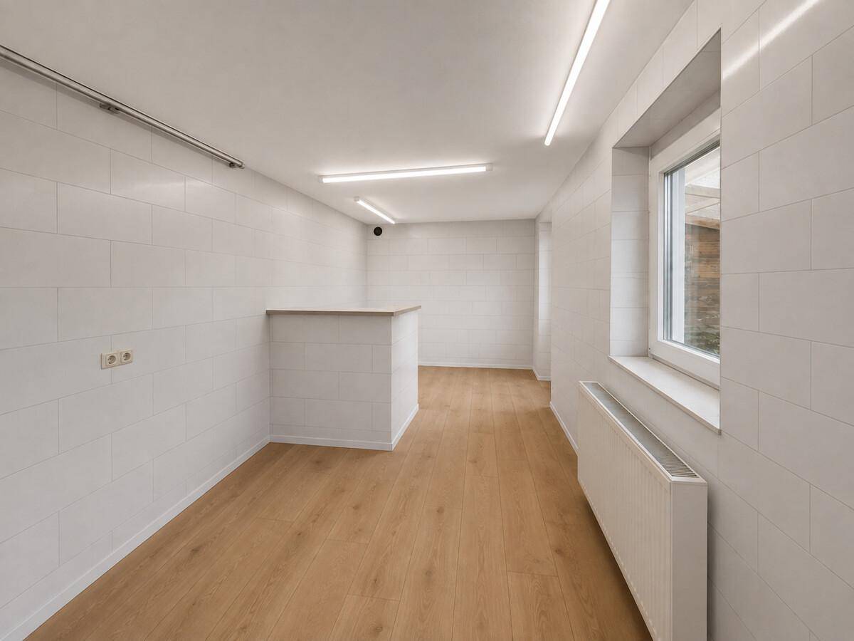 Heller, gefliester Raum mit Laminatboden, Fenster und einem kleinen Tresenbereich.