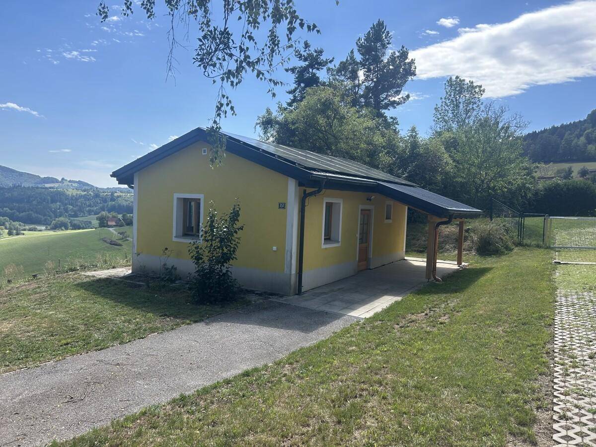 Seitenansicht eines gelben Hauses mit Solaranlage und überdachtem Eingangsbereich.