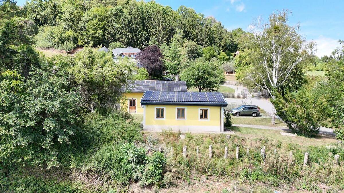 Luftaufnahme eines gelben Hauses mit Solaranlage, umgeben von viel Grün und Bäumen.